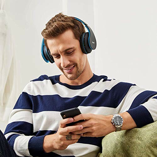 Man in striped sweater using headphones and smartphone.