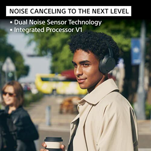 Person wearing noise-canceling headphones outdoors, holding a coffee.